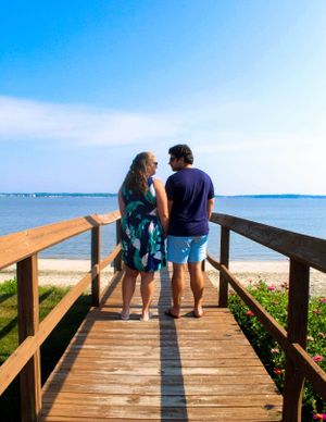 Two people standing together on a wooden boardwalk overlooking a peaceful beach view.