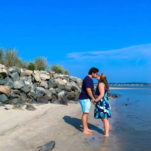 Couple standing together on a rocky beach with ocean waves in the background.