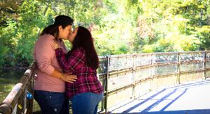Couple sharing an intimate moment on a wooden bridge surrounded by lush greenery.