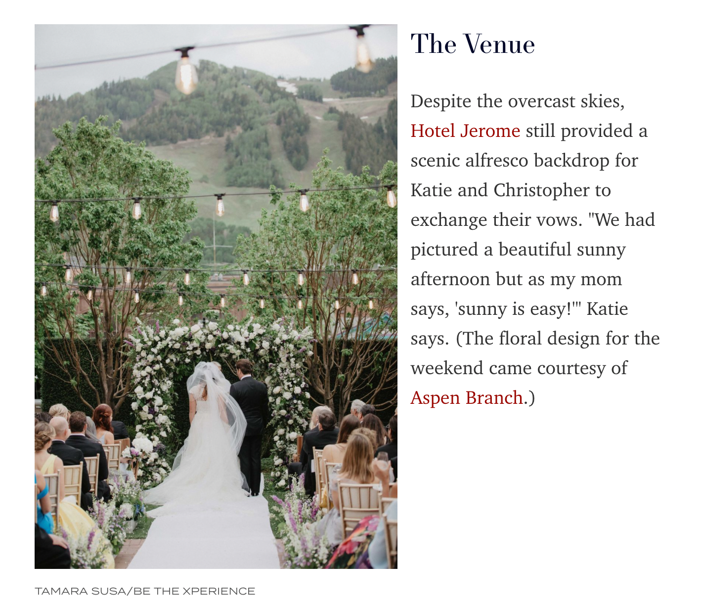 Outdoor wedding ceremony setup with floral arch and mountain backdrop under overcast skies.