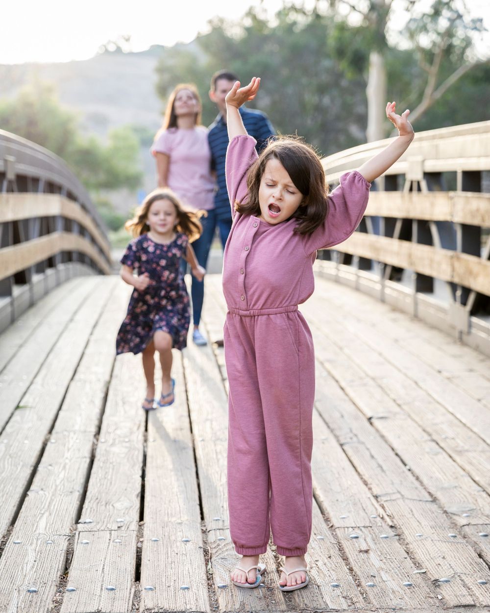 Orange County photographer captures Energetic young girl on a wooden bridge with family walking behind her.
