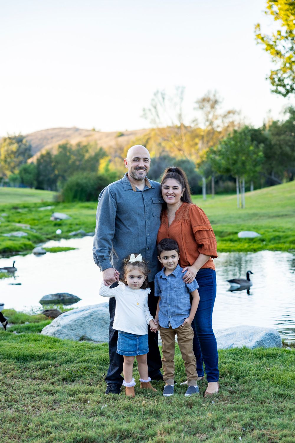 Orange County photographer captures Family of four smiling by a peaceful pond with ducks at golden hour.