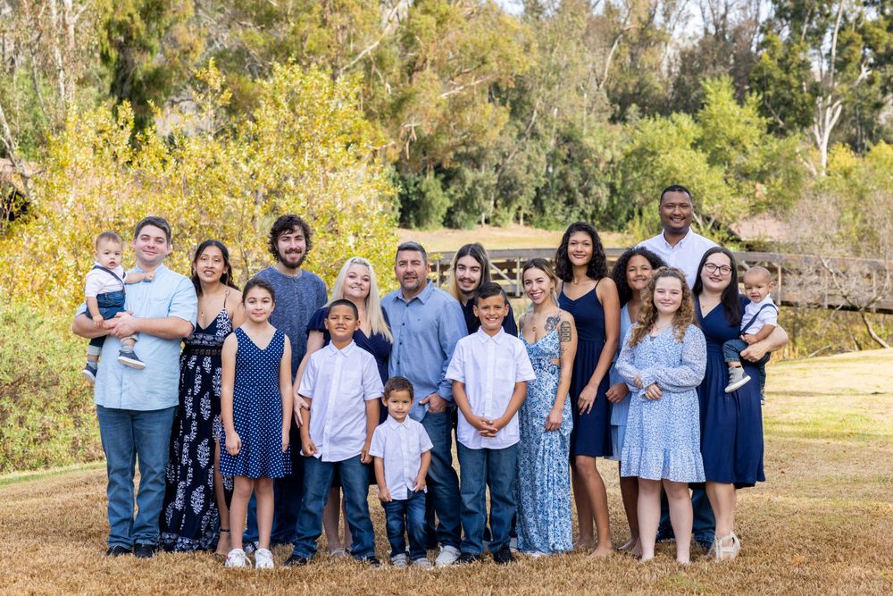 Orange County photographer captures Large extended family of about 20 members posing together outdoors in coordinating blue outfits.