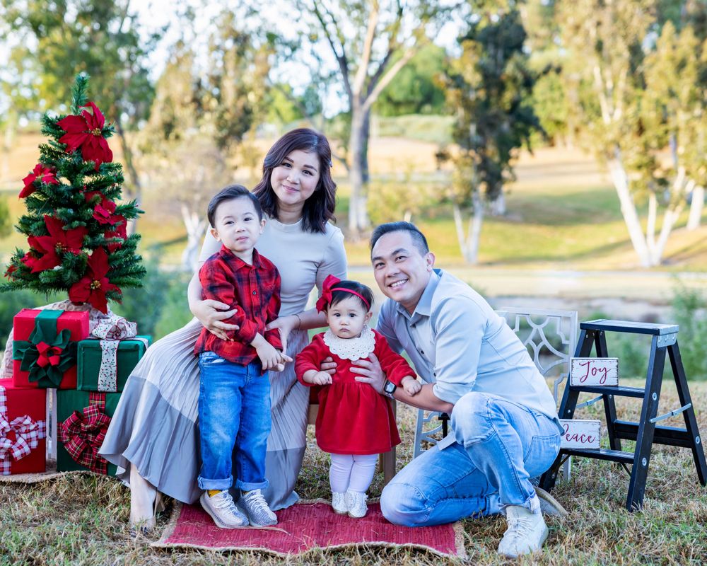 Orange County photographer captures  family with two toddlers posing with Christmas decorations in an outdoor park setting.
