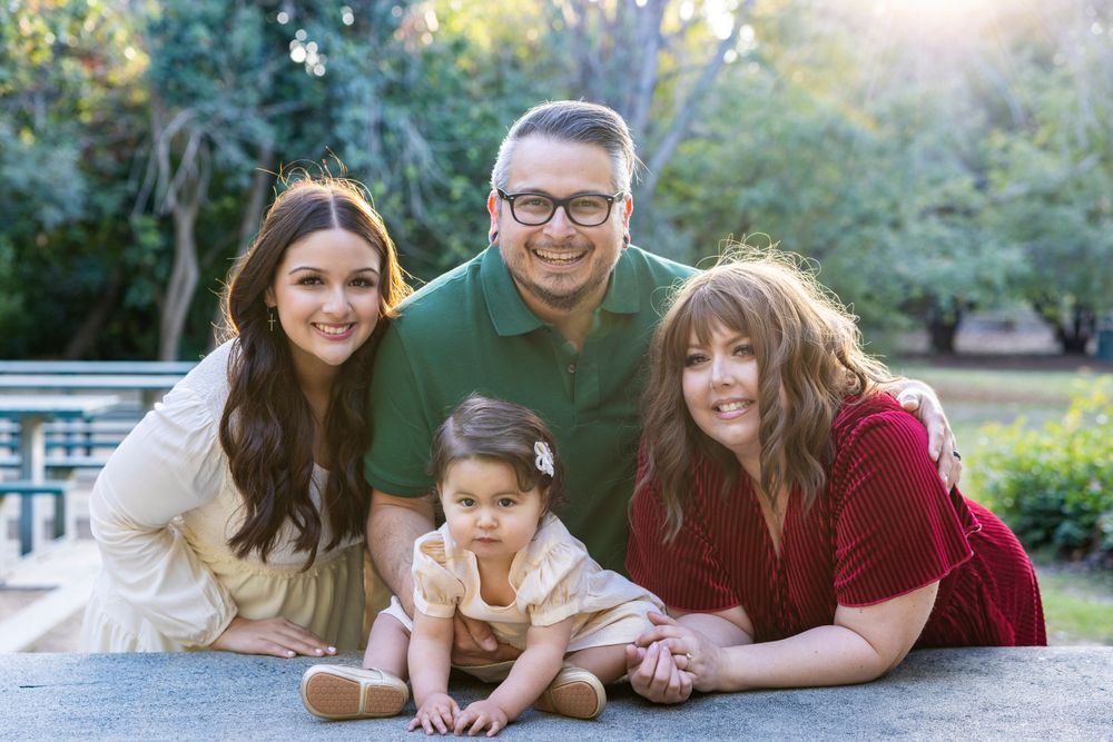 Orange County photographer captures Family of four with a baby girl posing together on a stone surface in a lush green park.