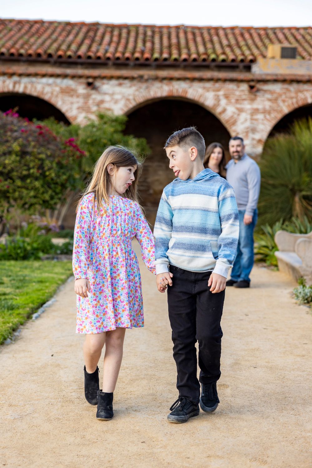 Orange County photographer captures Young siblings holding hands walking on a garden path at a historic Spanish mission.