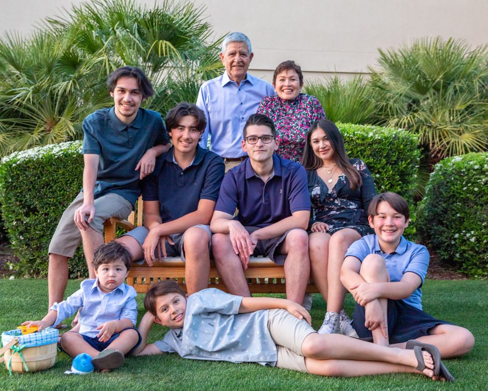 Orange County photographer captures Extended family portrait on a garden bench surrounded by palm trees outdoors.