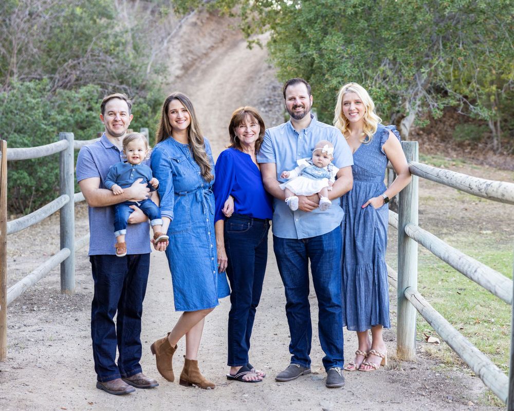 Orange County photographer captures Extended family of seven adults with two babies posing by a wooden fence on a dirt path.