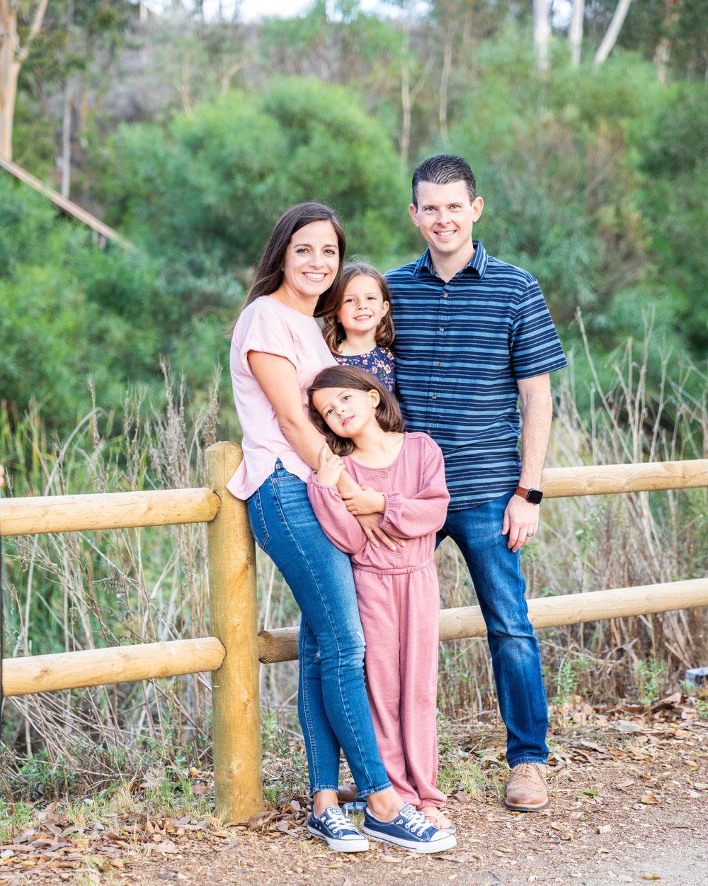 Orange County photographer captures Smiling family of four posing by a wooden fence in a nature park setting.