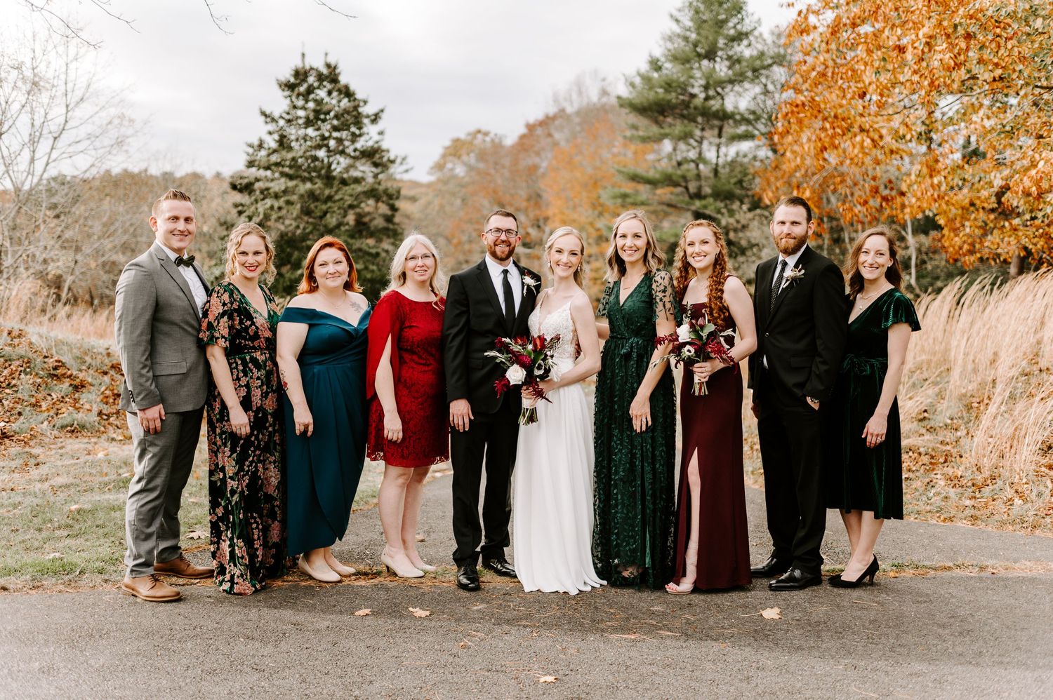 Wedding party group photo in autumn setting with burgundy and black color scheme.