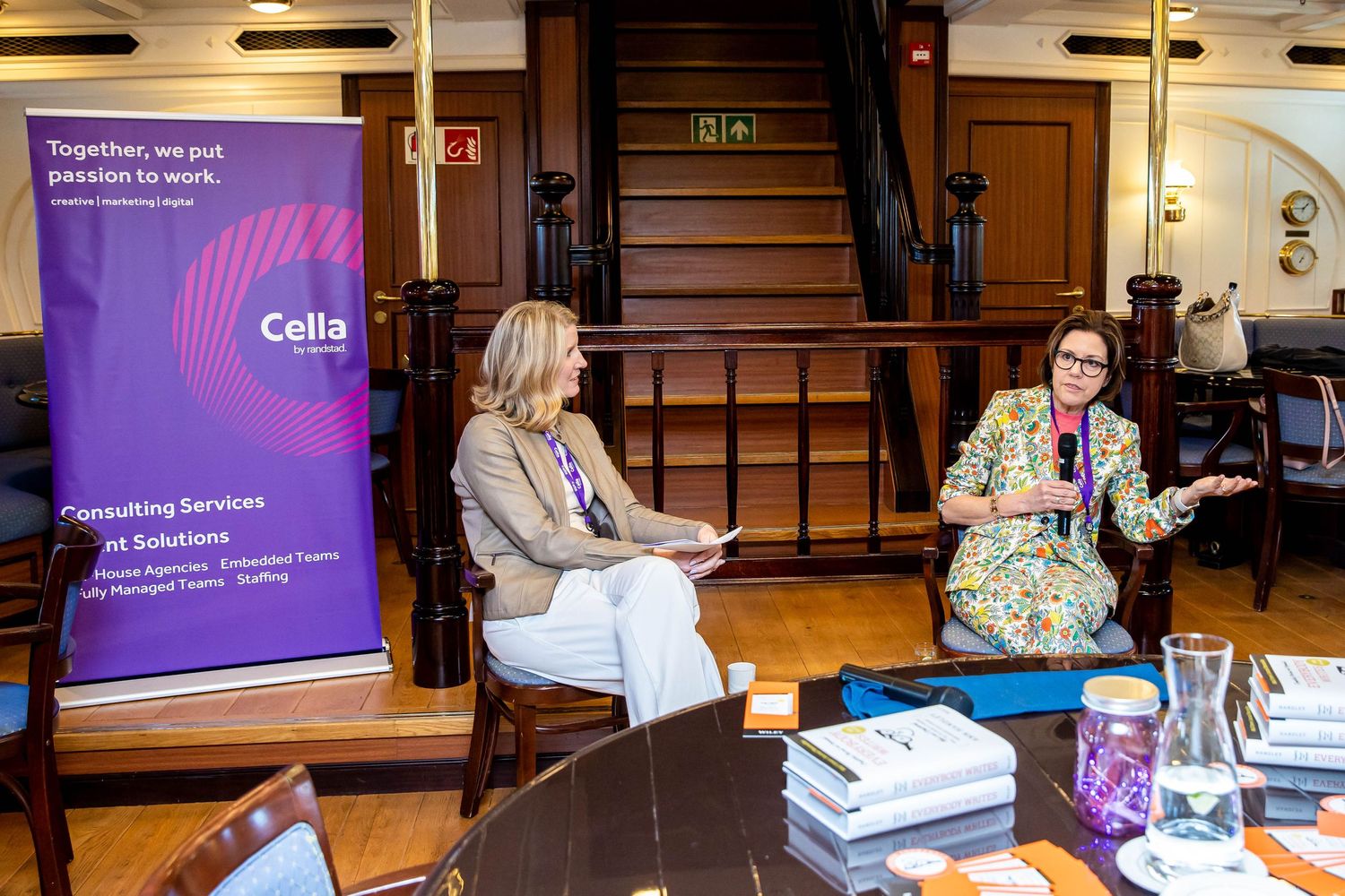 Two professionals having discussion at conference with purple banner and books on table.