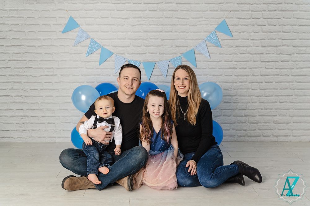 Portrait session with blue balloons and bunting against white brick wall background.