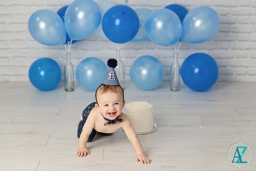 Blue balloon photo setup with crawling baby wearing party hat.
