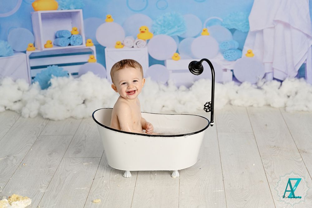 Whimsical bath photography setup with bubbles and rubber ducks on wood floor.