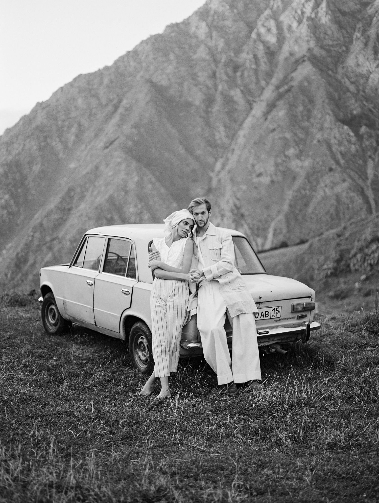 Engaged couple standing at a vintage car on top of the mountains in the Kazbegi region of the Republic of Georgia.