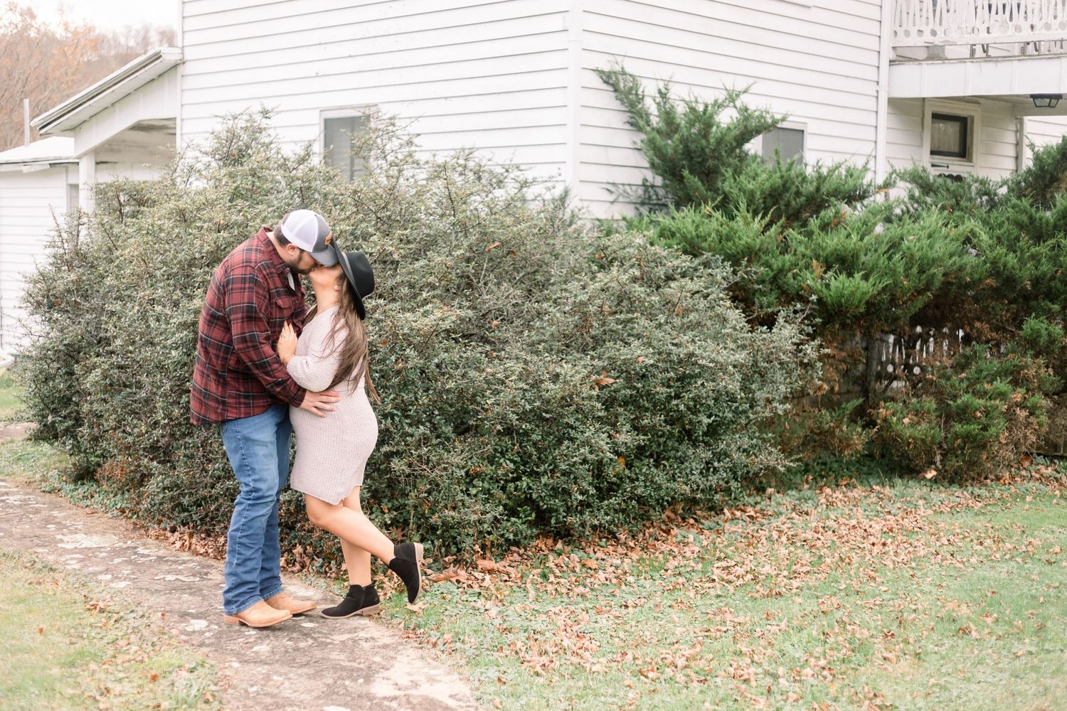 A couple playfully poses in a garden with autumn leaves scattered on the ground.