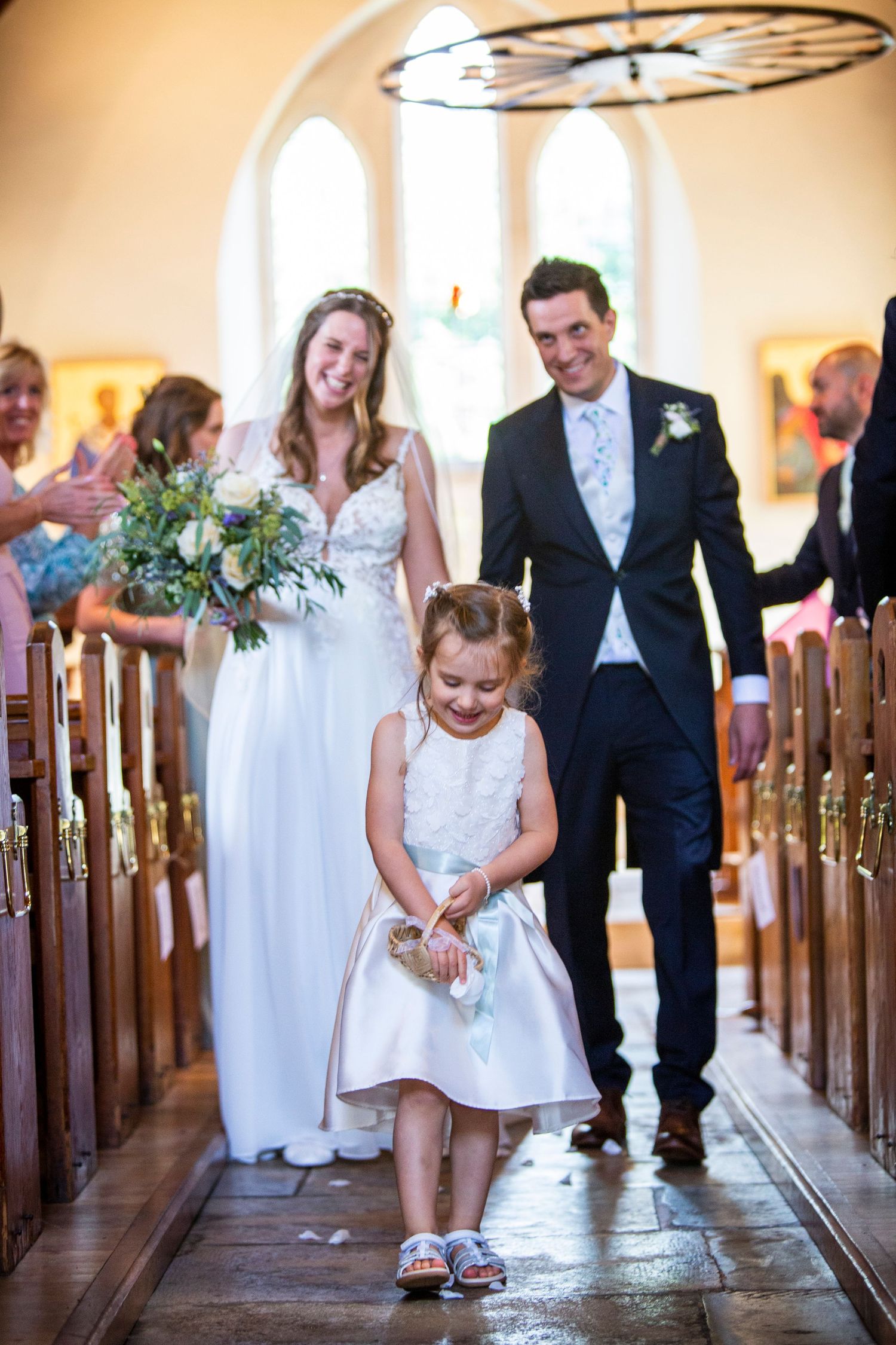 Young flower girl walks down church aisle during wedding ceremony.