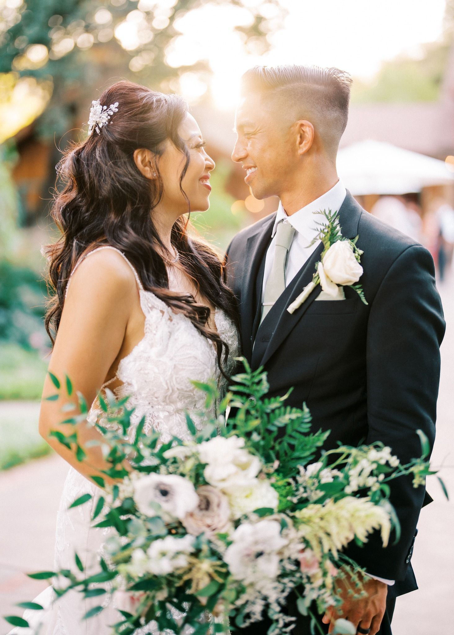 Romantic sunset portrait of newlyweds with lush green foliage and white floral bouquet.