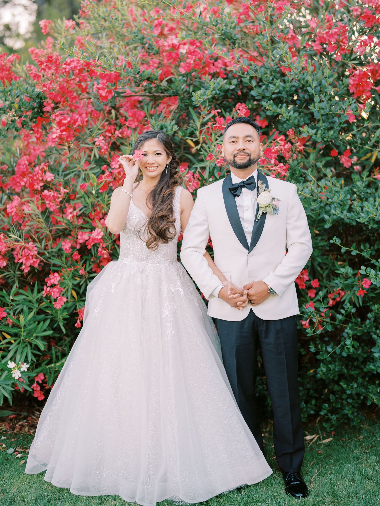 A elegant wedding portrait framed by blooming red bougainvillea in a garden setting.