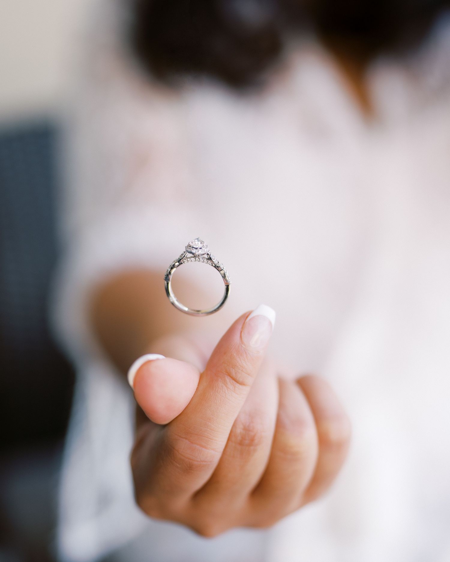A close-up of a diamond engagement ring held up by a manicured hand.