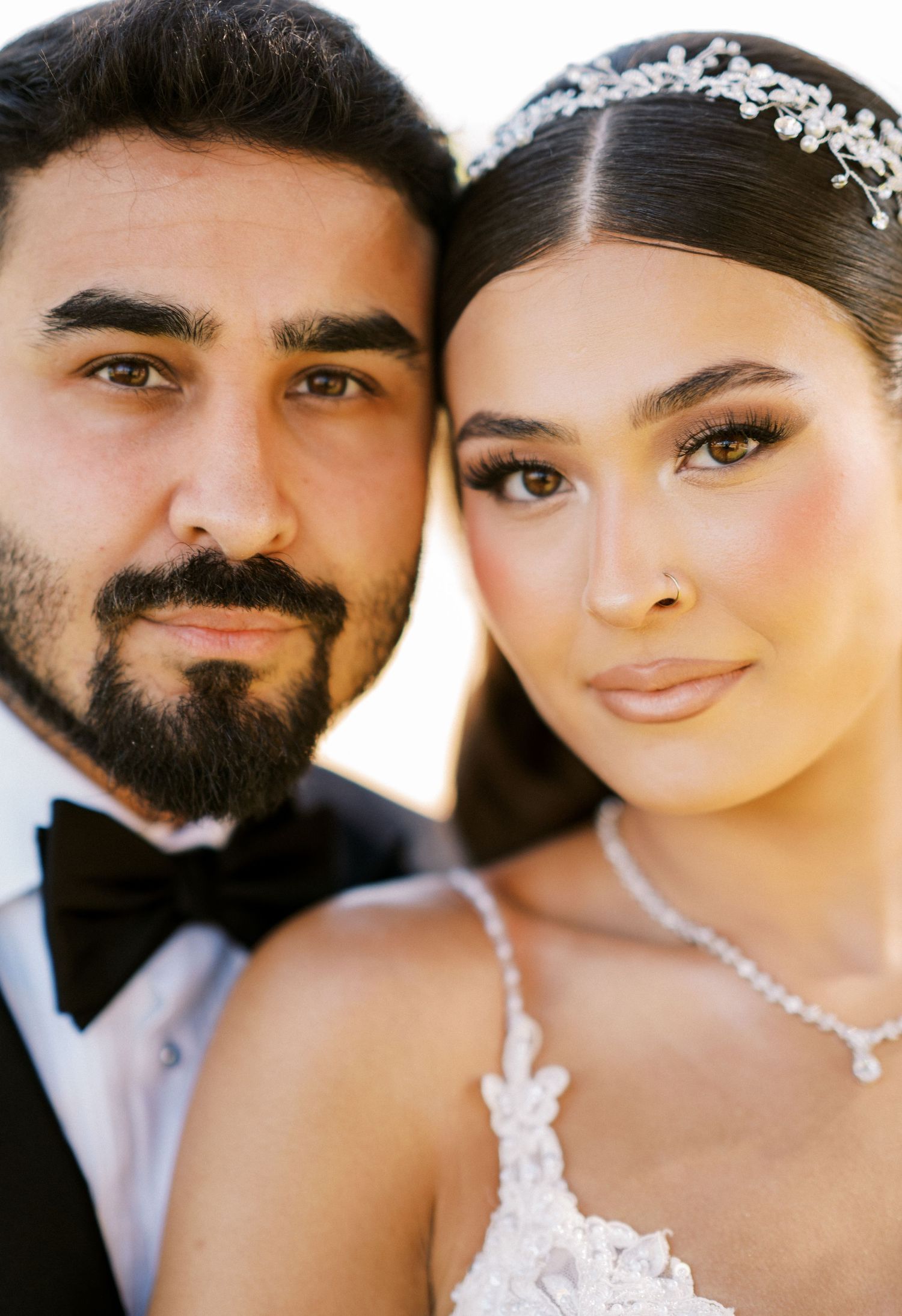 A close-up wedding portrait capturing an intimate moment against a sunlit backdrop.