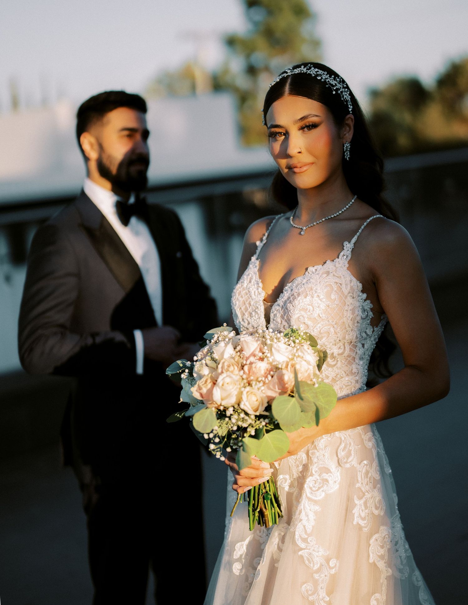 An artistic wedding portrait with the bride holding a blush bouquet in golden hour light.