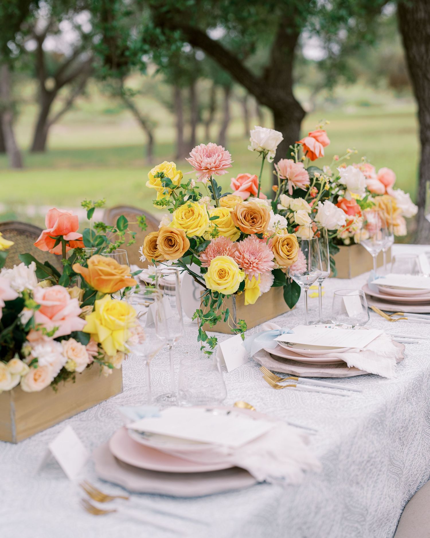 Elegant garden reception table with yellow and coral floral centerpieces and crystal glassware.