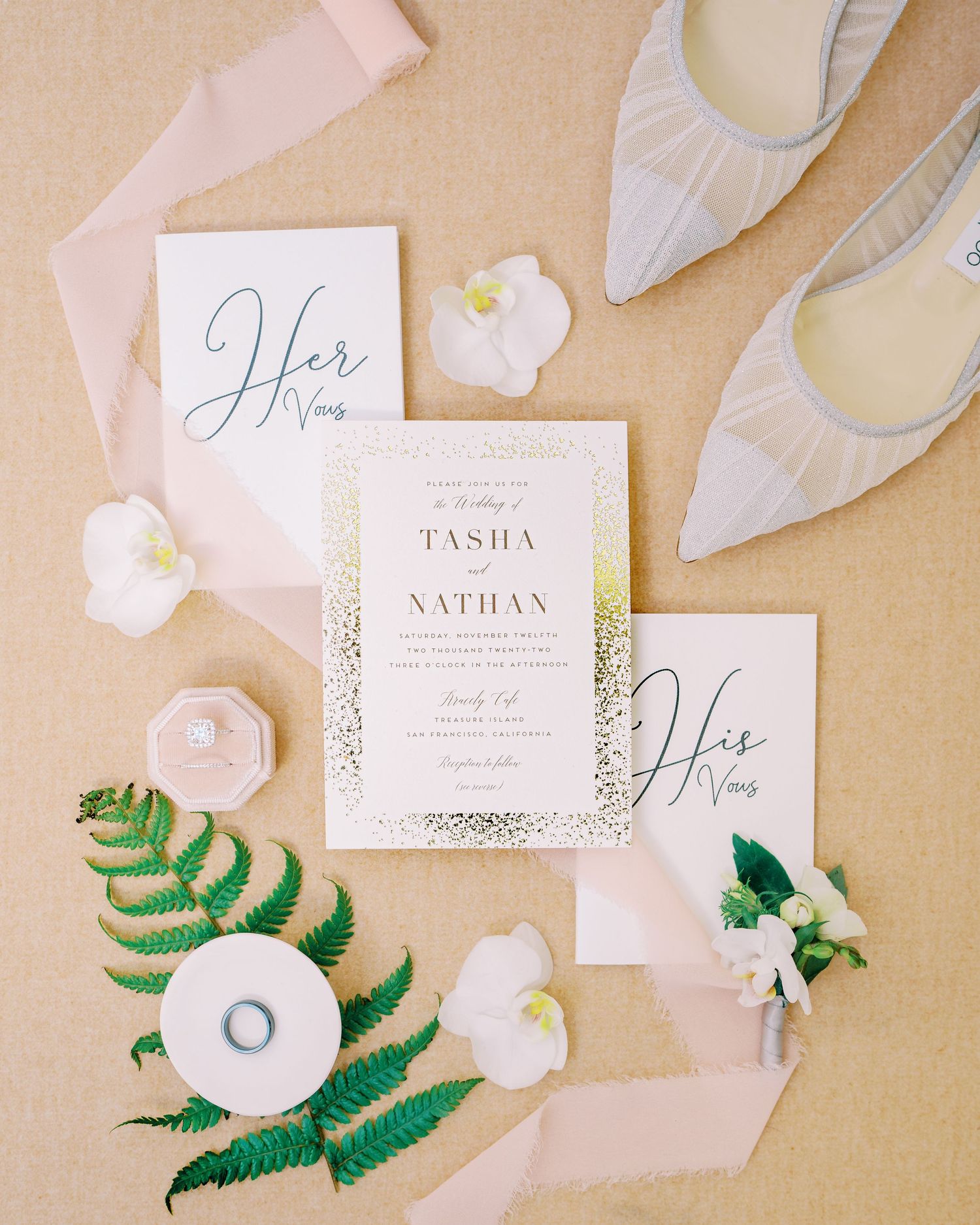 Wedding invitation suite with greenery and white flowers laid out on beige linen with bridal shoes.