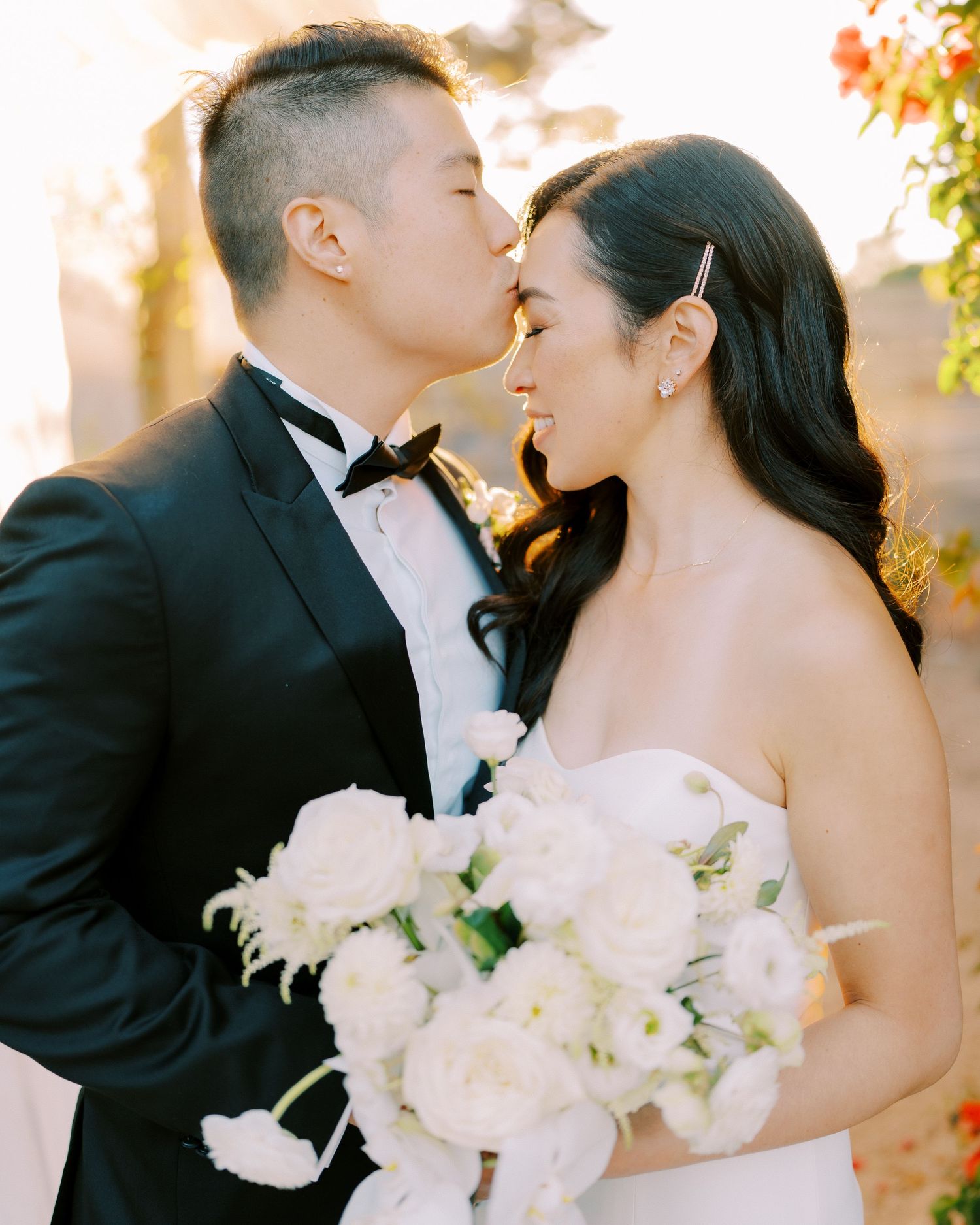 Elegant wedding portrait with bride holding white bouquet and groom in classic black tuxedo.