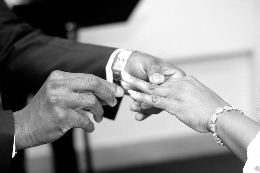 Close-up black and white photo of hands exchanging wedding rings during a ceremony.