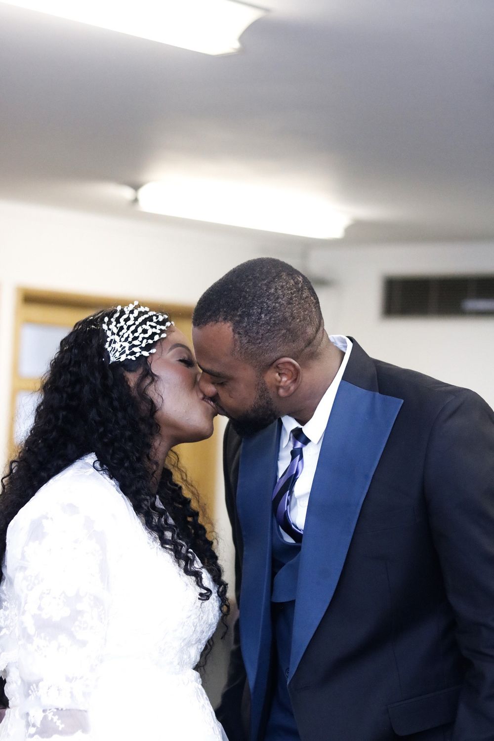 Intimate wedding moment captured in indoor setting with decorative headpiece and formal attire.