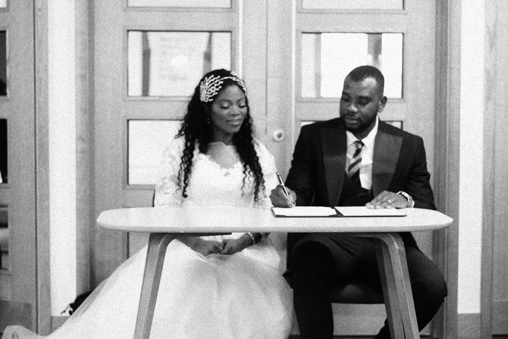 Black and white photo of couple signing marriage documents at ceremony table.