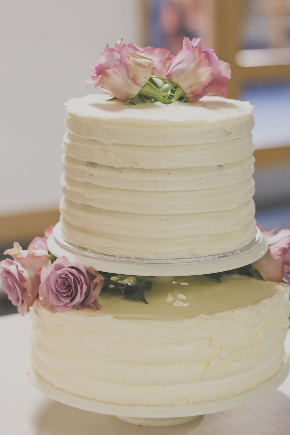 Two-tier white wedding cake decorated with pink roses and textured frosting.