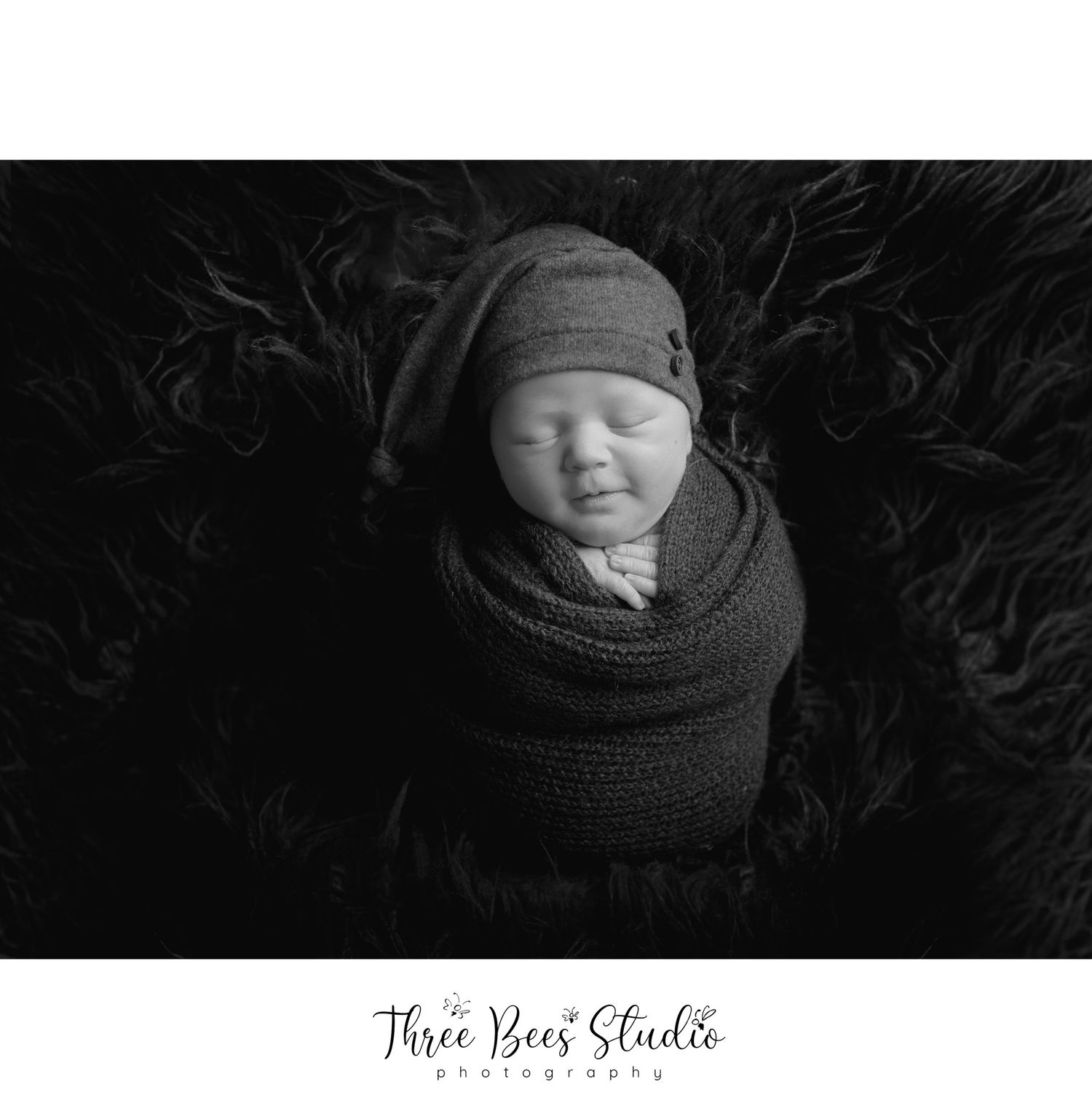 Black and white portrait of sleeping newborn wrapped in knit fabric with matching hat.