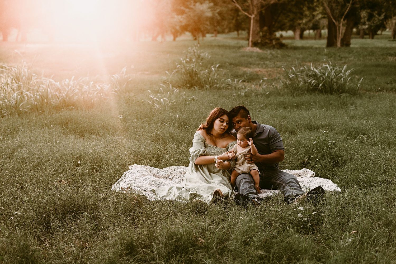 Family sitting together on a blanket during a golden hour photo session in a park.