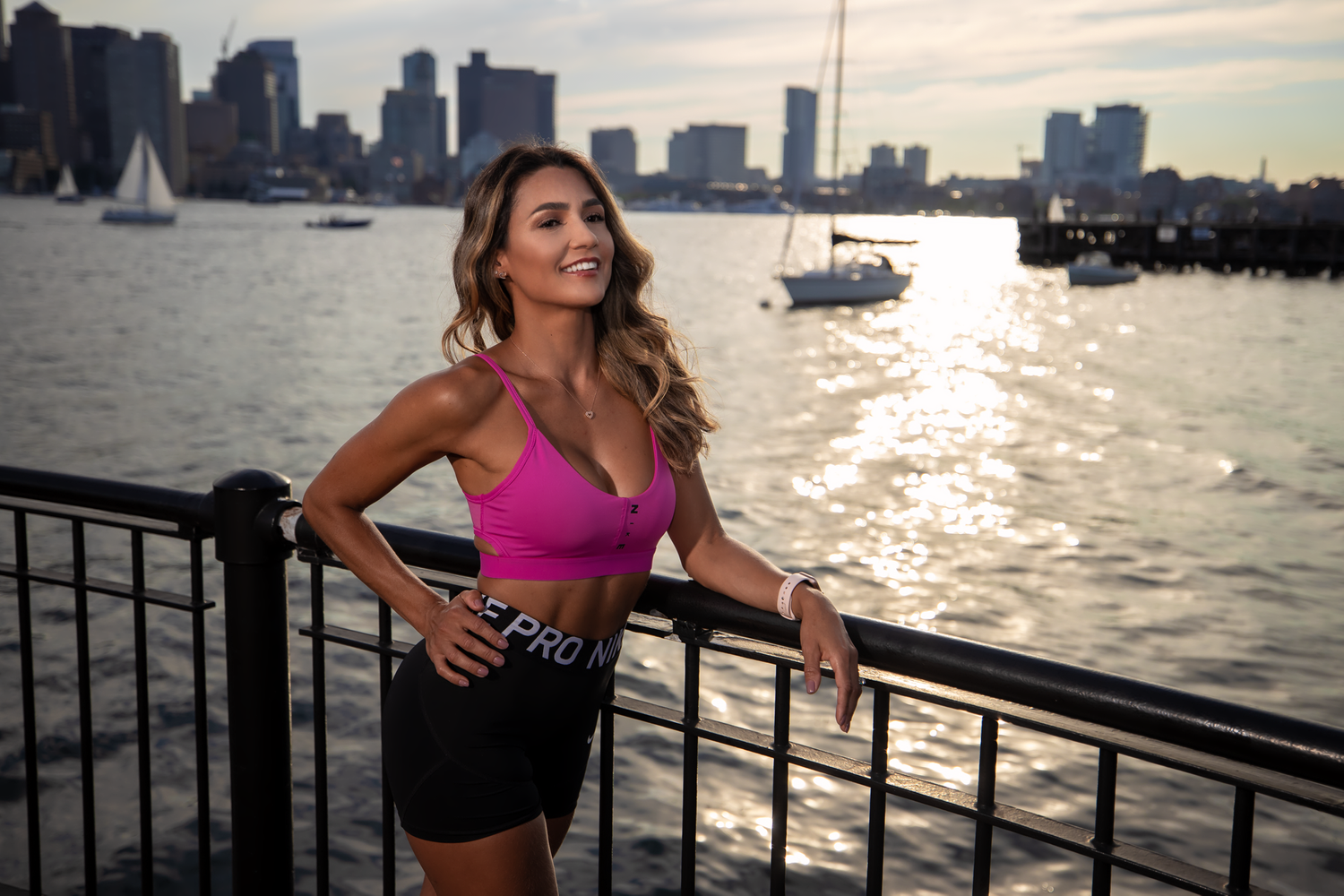 Fitness photoshoot along waterfront with city skyline at sunset.