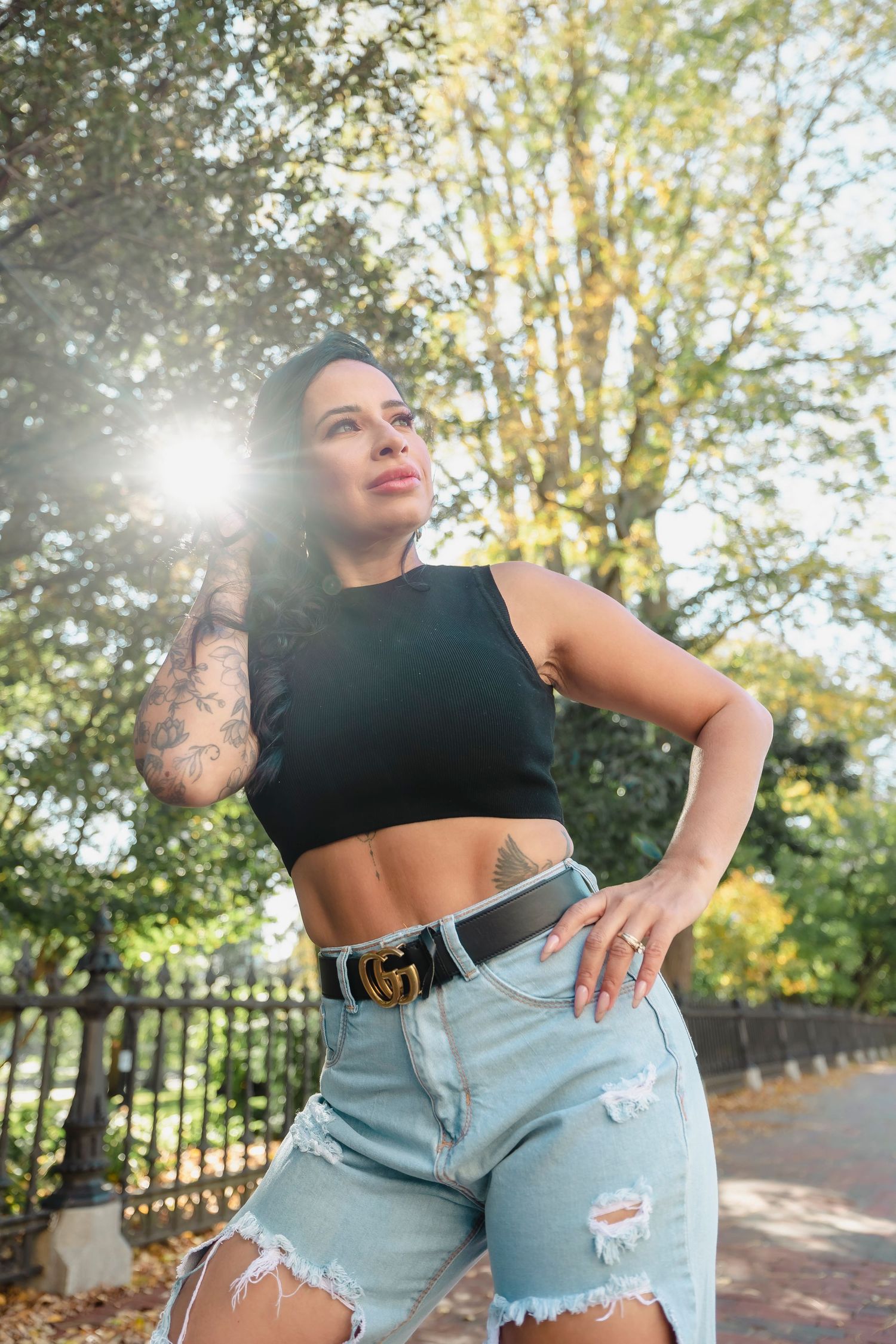 Sun-drenched outdoor photoshoot with distressed denim and casual black top.