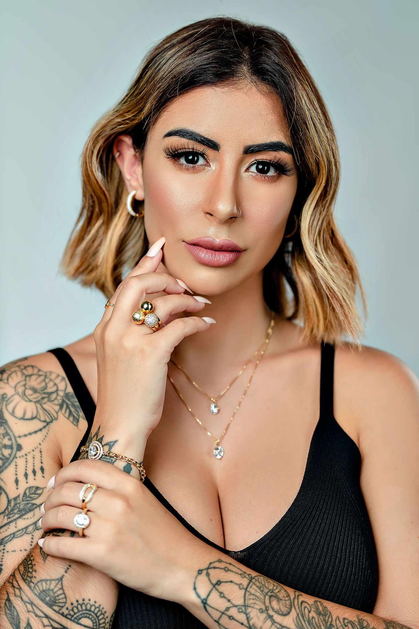 Studio beauty portrait showcasing tattoo art and layered necklaces against gray background.