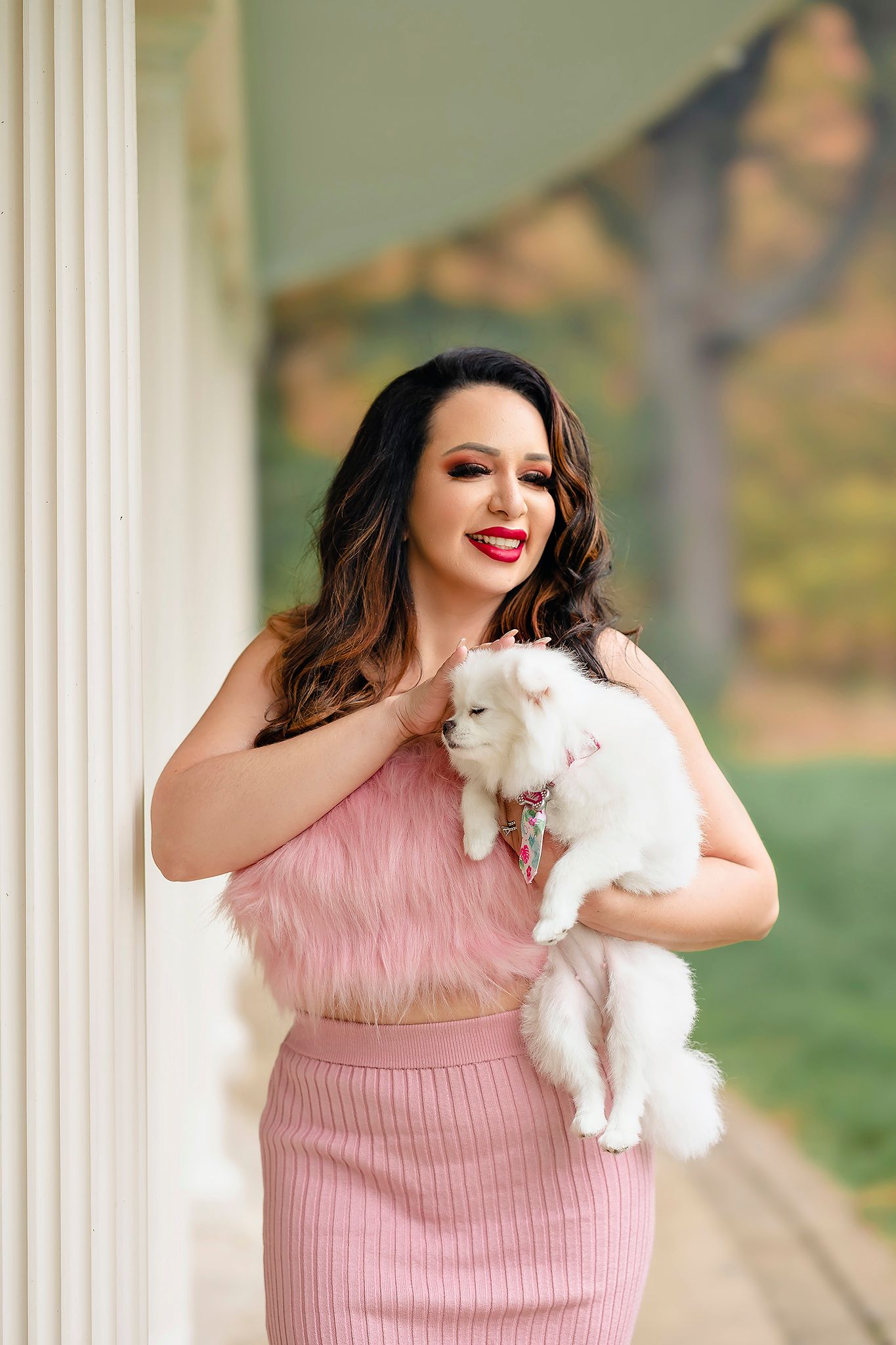 Lifestyle portrait with white fluffy cat in pink outfit against architectural backdrop.