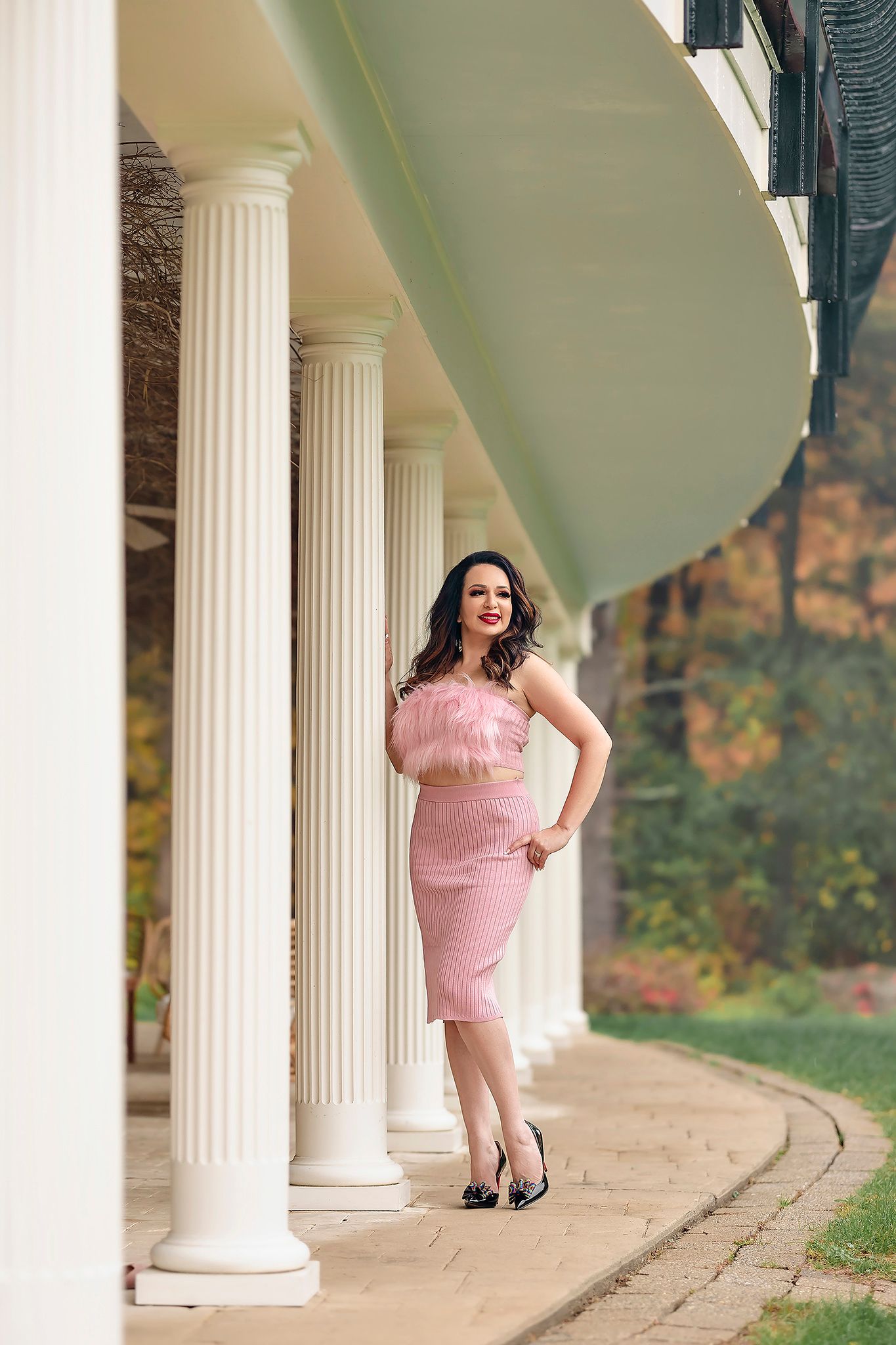Elegant fashion photo with pink dress against classical columns and autumn scenery.