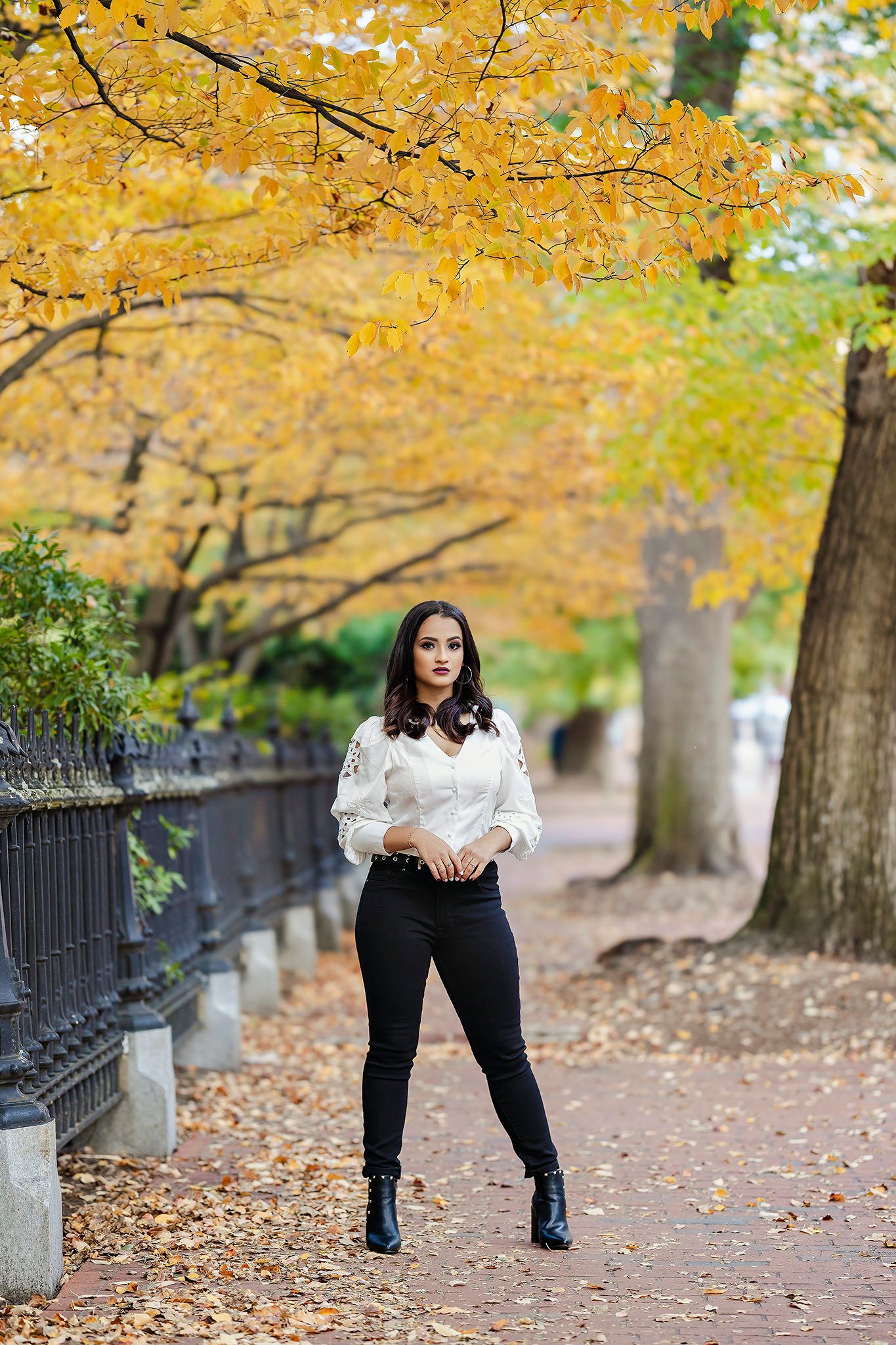 Person in black and white outfit walking through autumn park with fallen leaves.