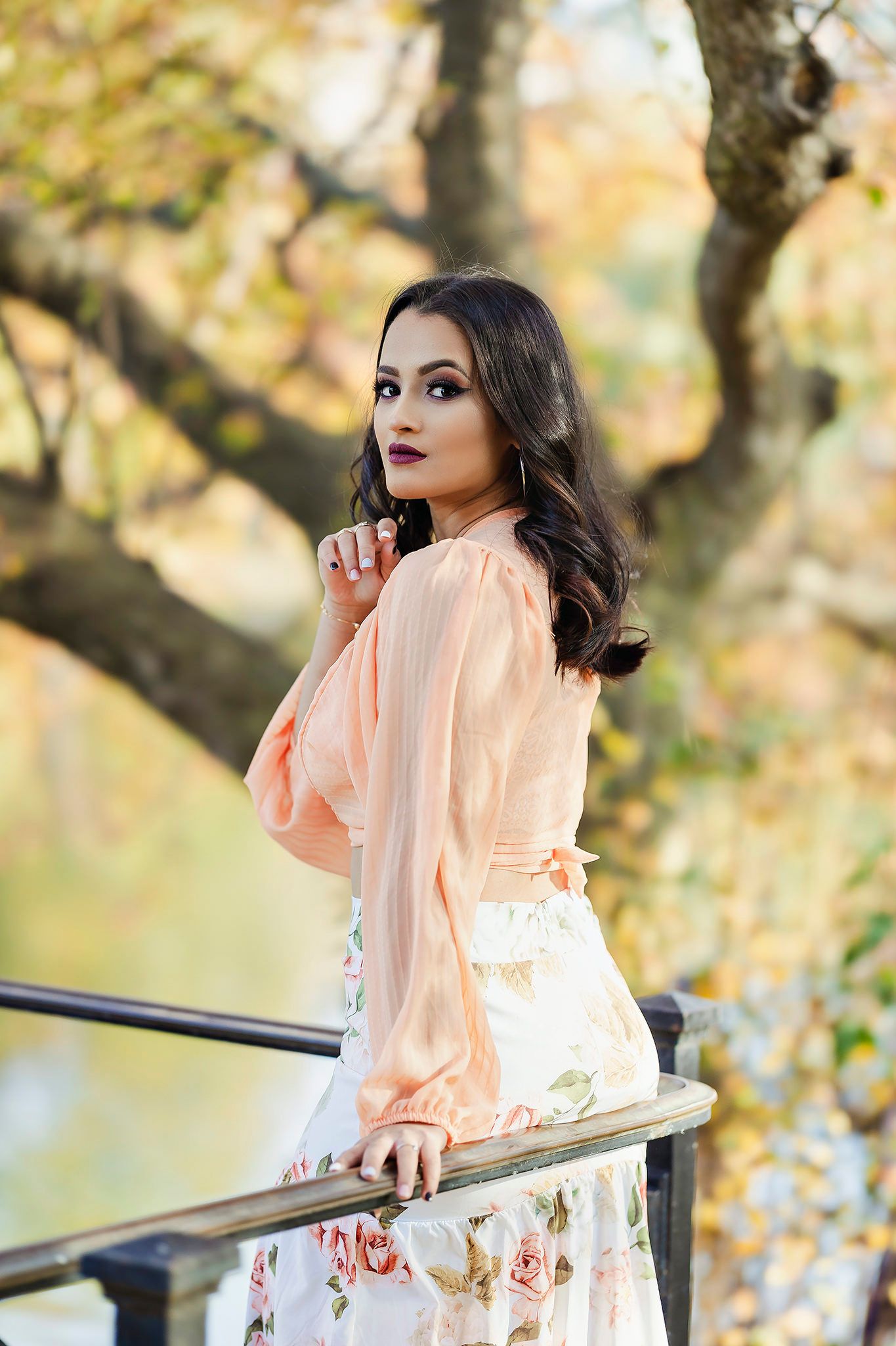 Person in peach dress posing against autumn foliage background.