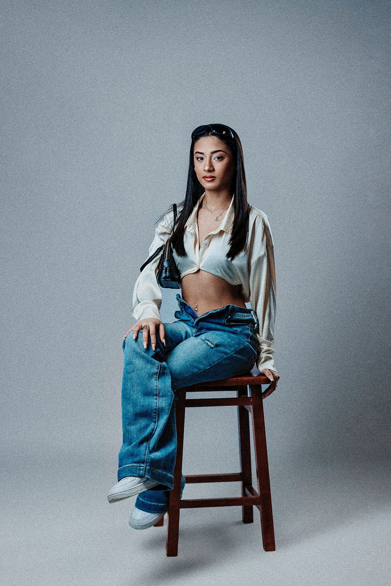 Minimalist studio portrait with white shirt and jeans on wooden stool.