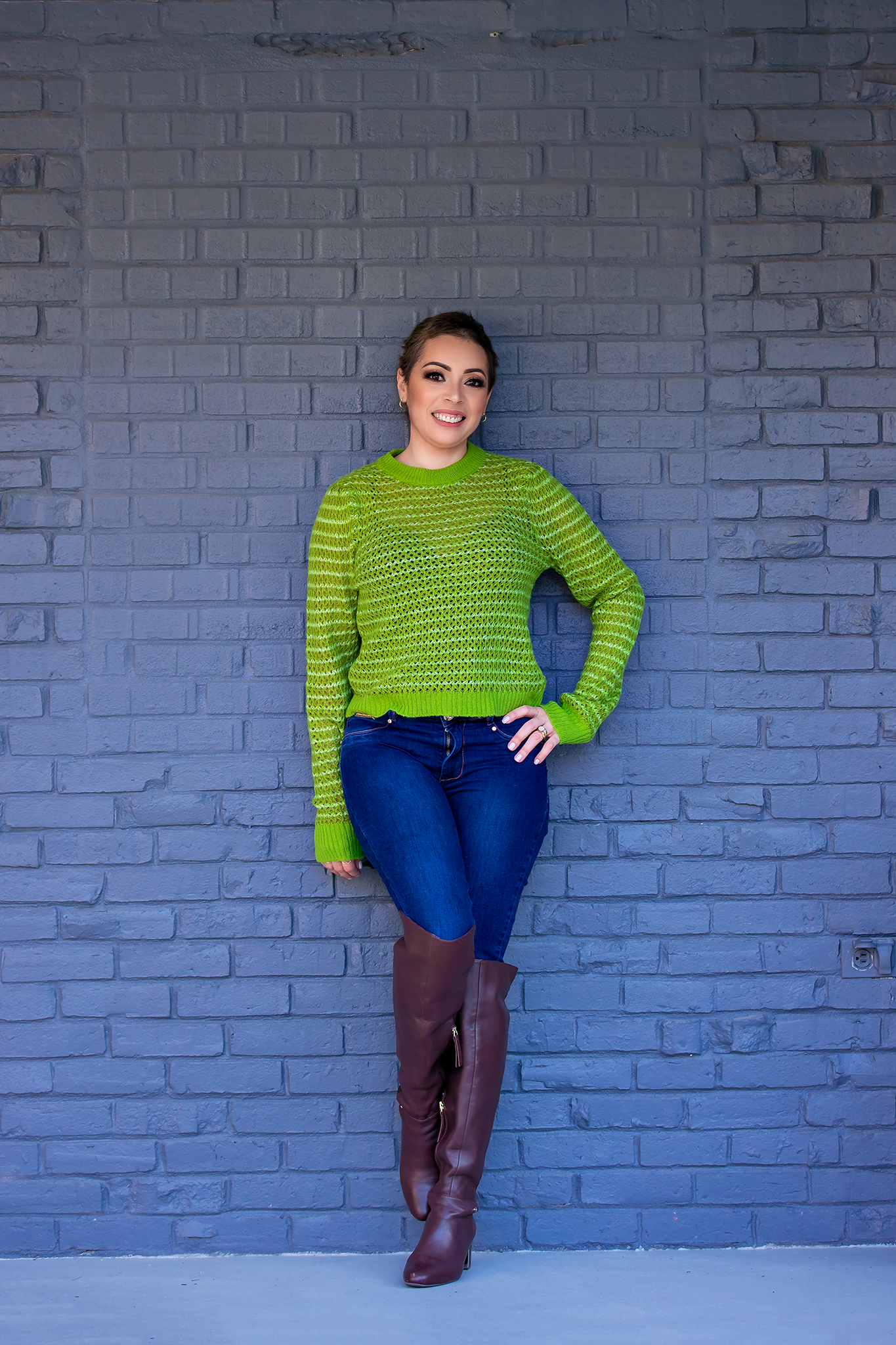 Fashion photo against purple brick wall featuring bright green sweater, jeans and brown boots.
