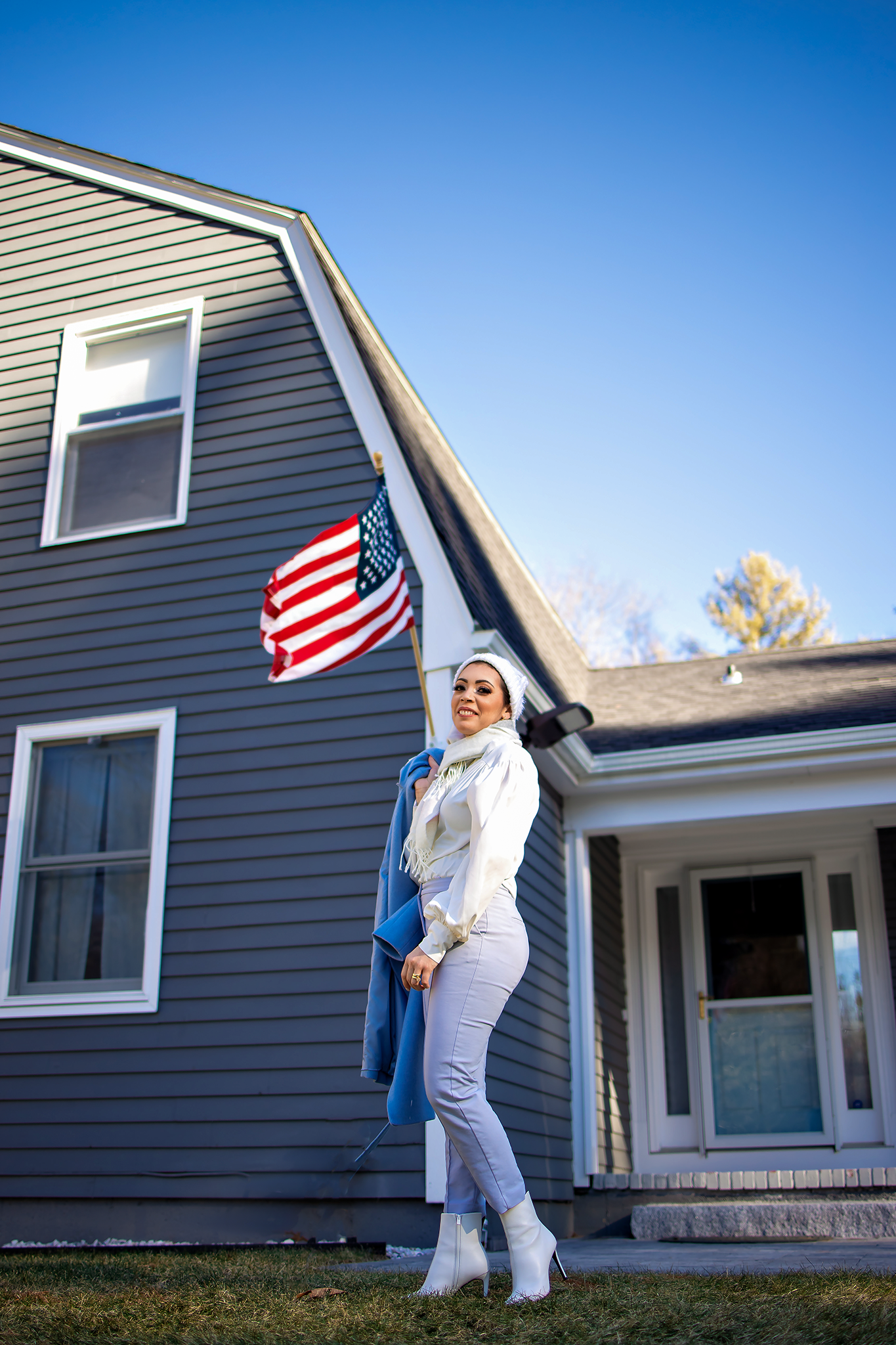 Casual fashion poses with American flag against navy blue house siding on sunny day.
