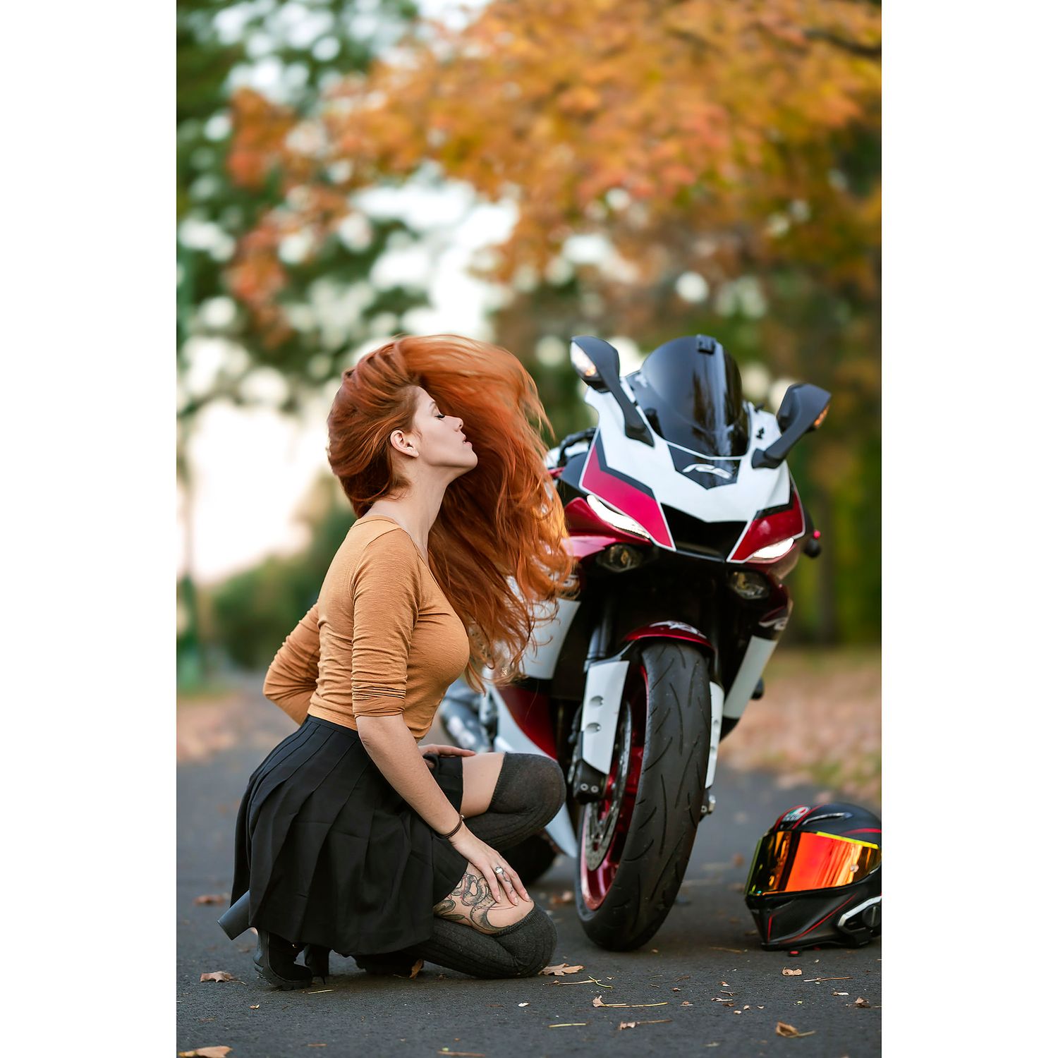 Person posing with sport motorcycle amid autumn foliage.