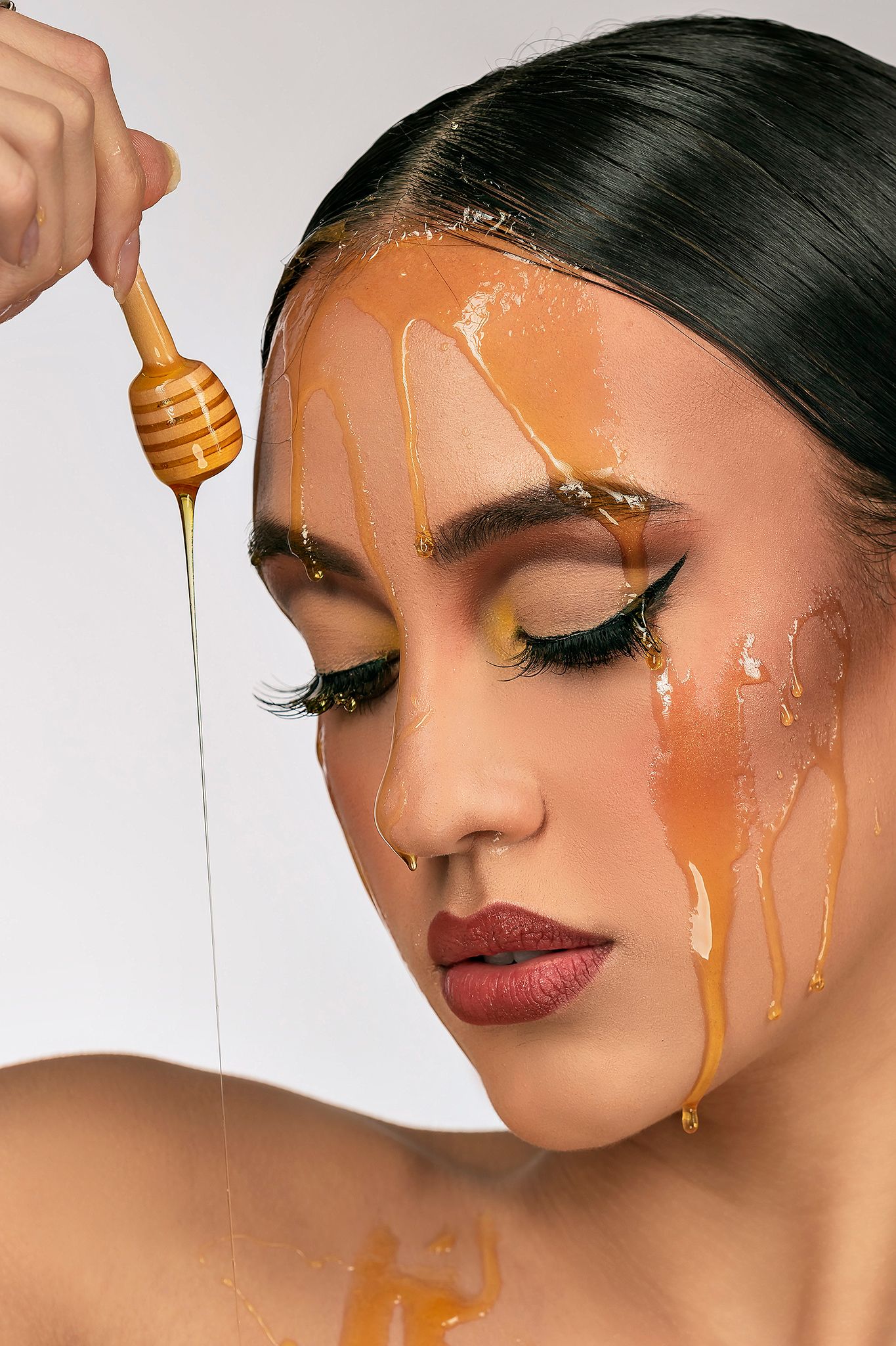 Artistic beauty photograph with honey dripping over face and gold-toned eye makeup.