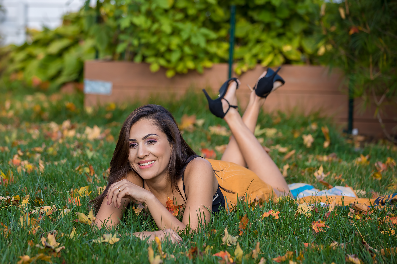 Person lying on grass with scattered autumn leaves during outdoor photo session.