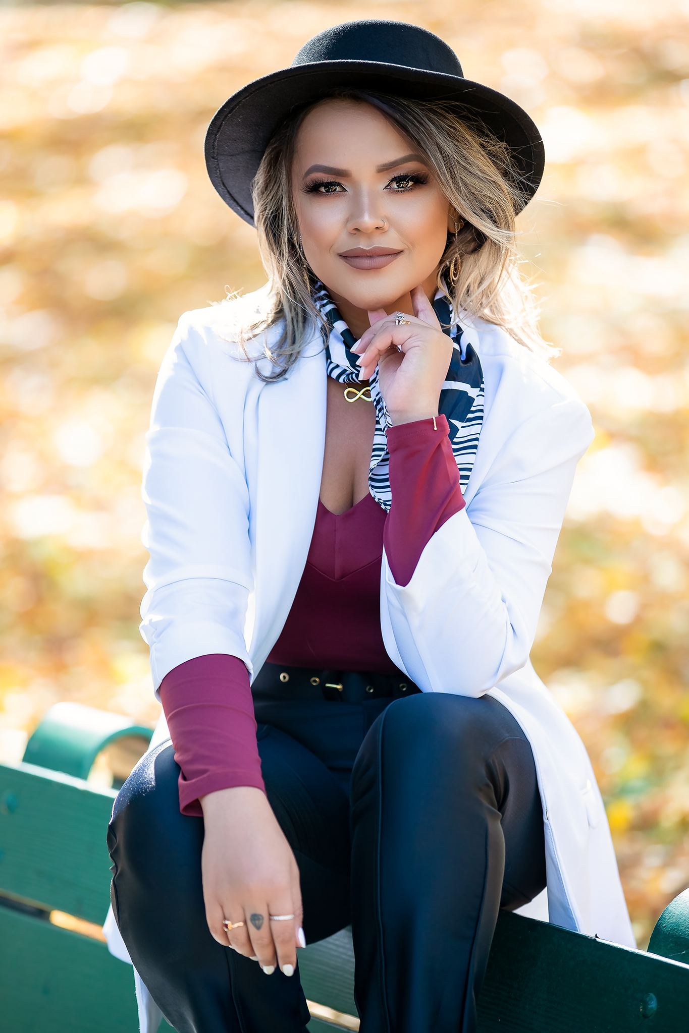 Portrait session on park bench with white blazer and burgundy top during fall season.
