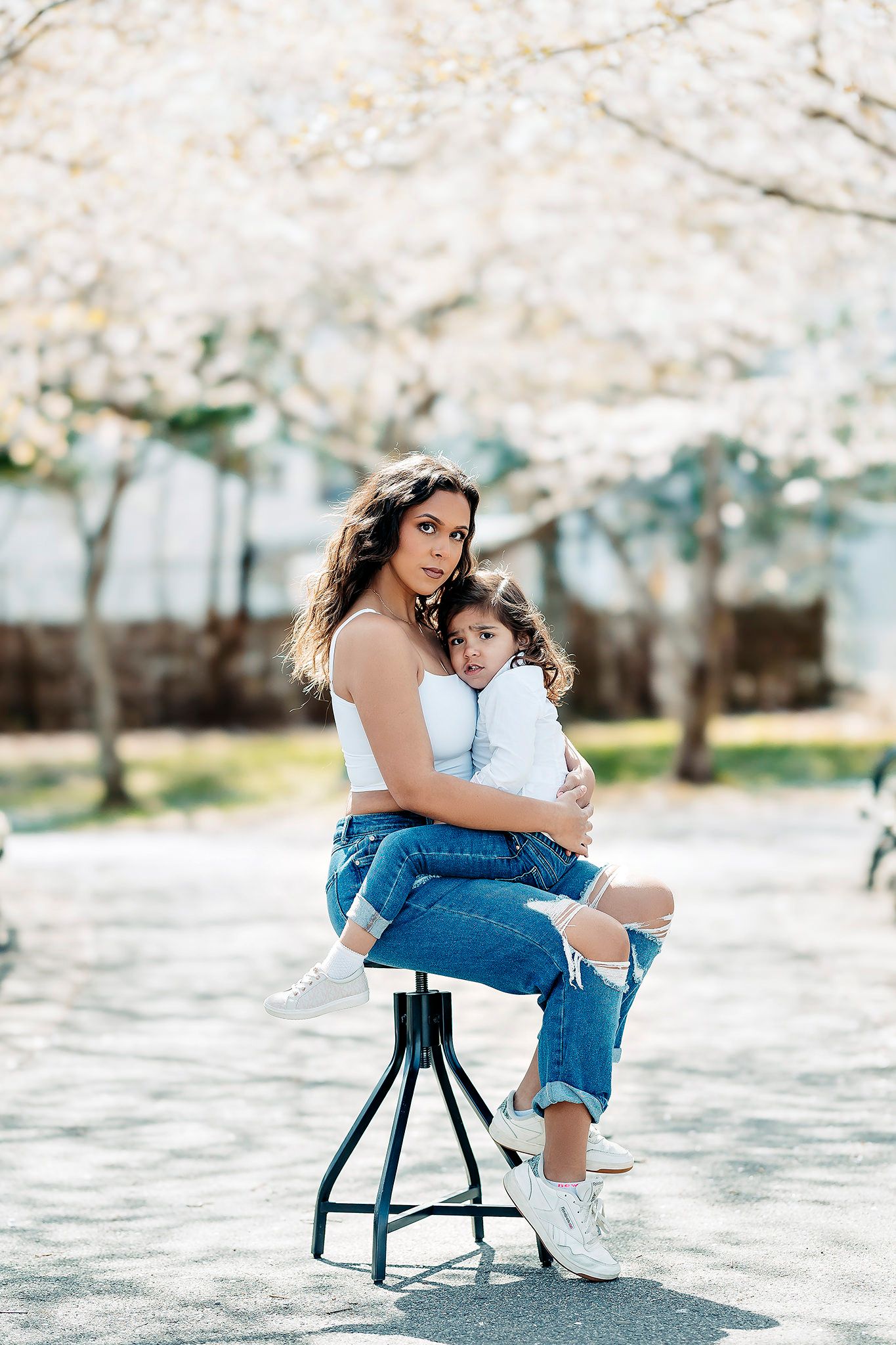 Spring photoshoot with cherry blossoms featuring casual denim look on a wooden stool.